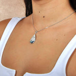 Abalone, white topaz, and sterling silver pendant featuring a sun and wave design, worn by a model. 