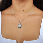 Abalone, white topaz, and sterling silver pendant featuring a sun and wave design, worn by a model. 