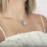 In this photo there is a model turned to the right with blonde hair and a white shirt with purple flowers, wearing a sterling silver anthurium pendant.