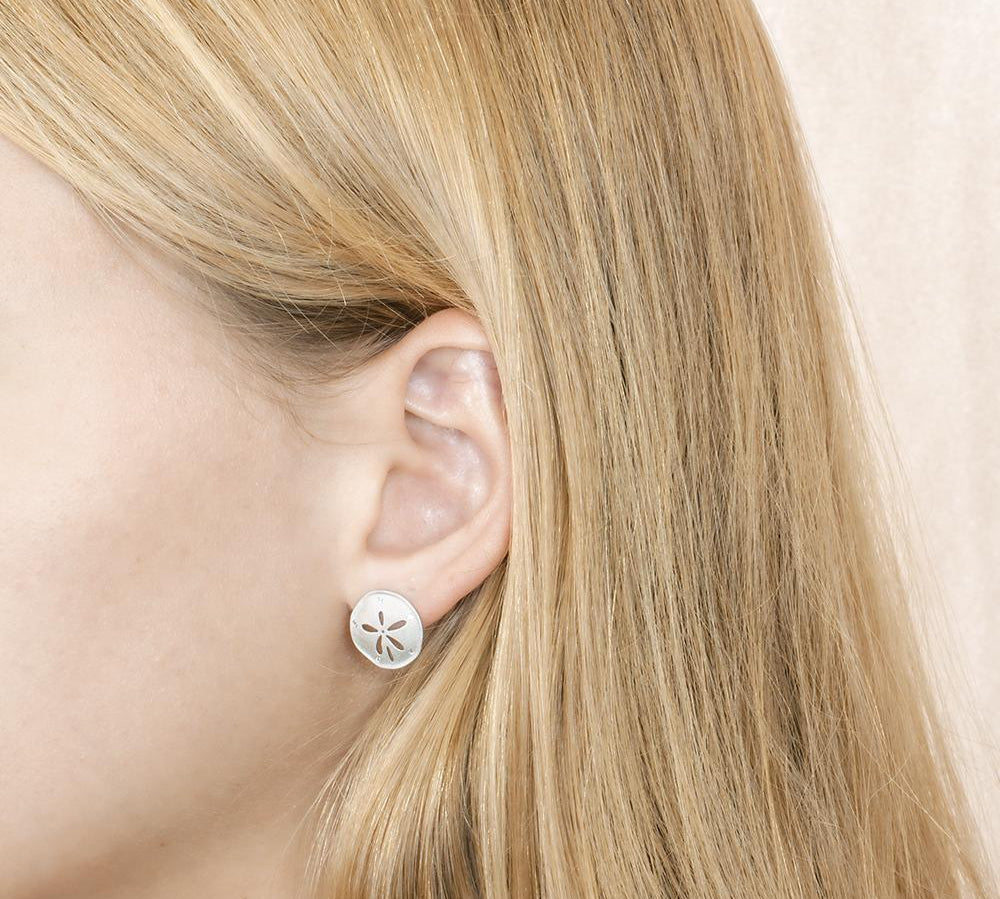 The picture shows a model wearnig a 925 sterling silver sand dollar stud earring with topaz.
