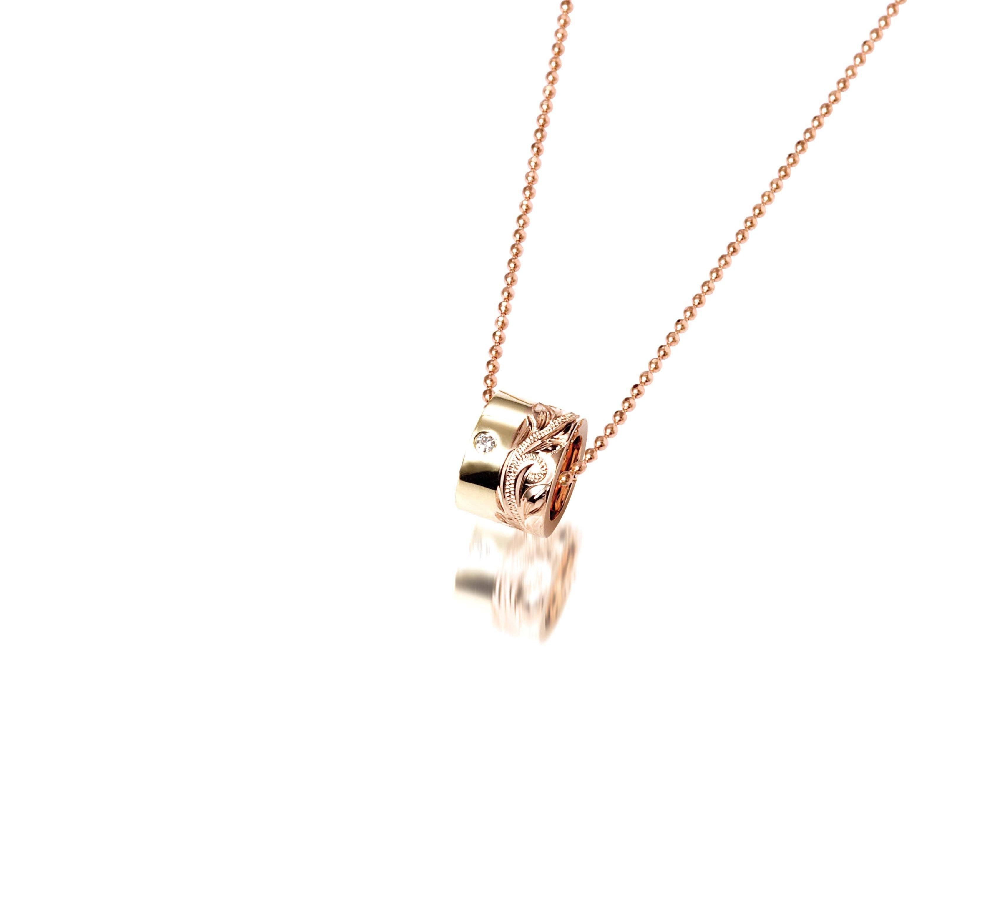 This picture shows a 14k yellow and rose gold two-tone barrel pendant with hand engravings and a diamond.