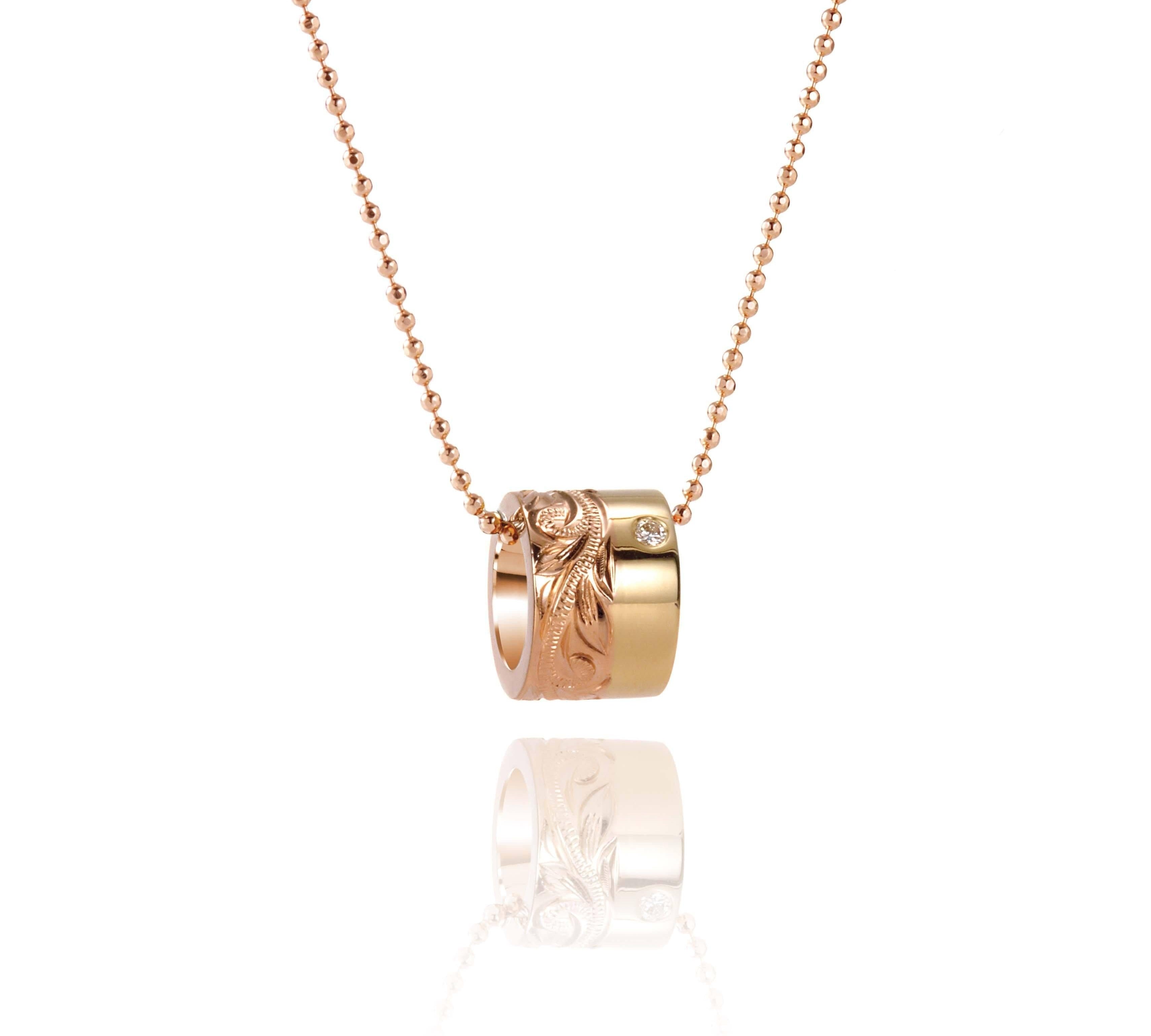 This picture shows a 14k yellow and rose gold two-tone barrel pendant with hand engravings and a diamond.