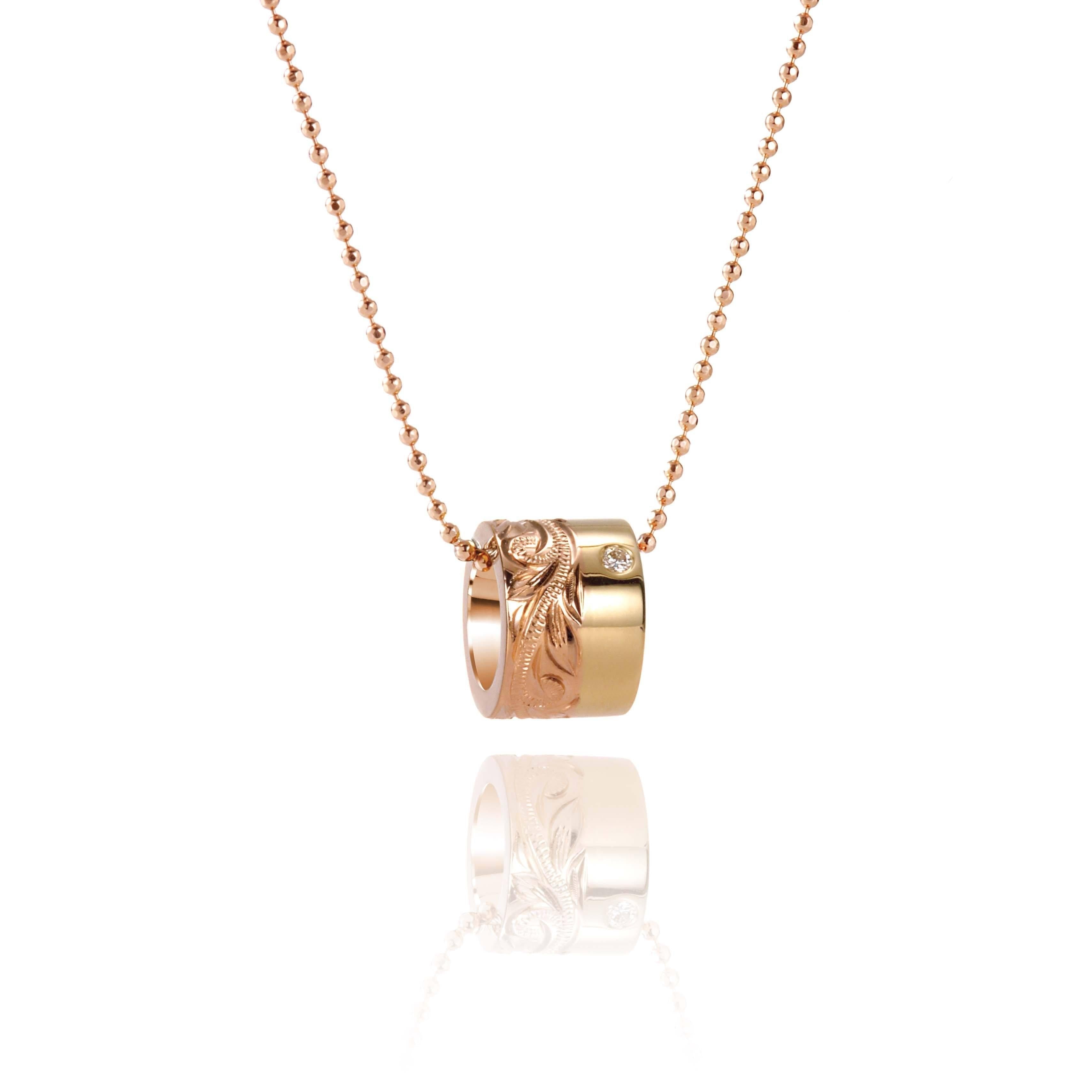 This picture shows a 14k yellow and rose gold two-tone barrel pendant with hand engravings and a diamond.