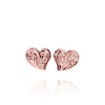 In this photo there is a pair of 14k rose gold heart stud earrings with plumeria flower engravings.