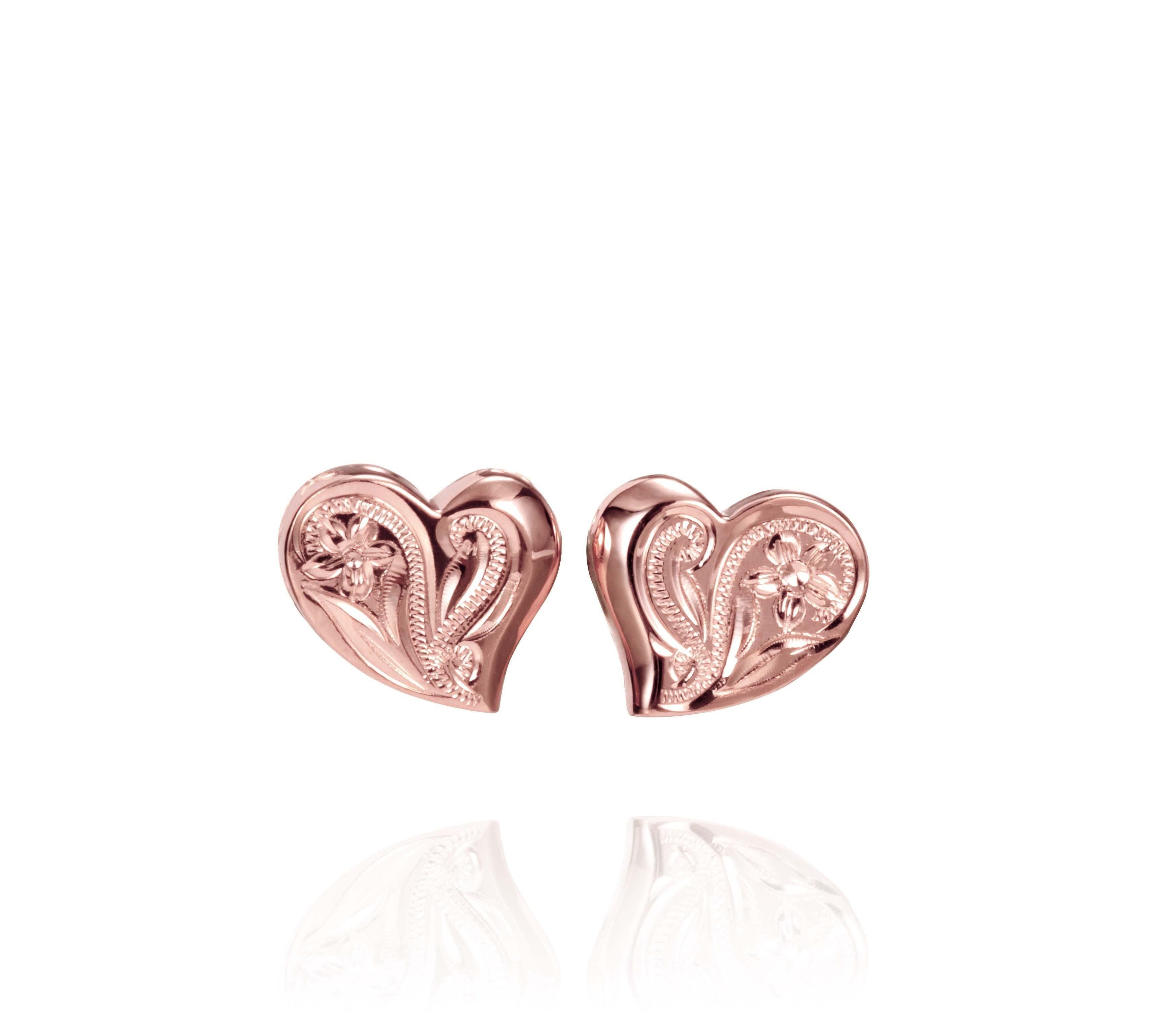 In this photo there is a pair of 14k rose gold heart stud earrings with plumeria flower engravings.