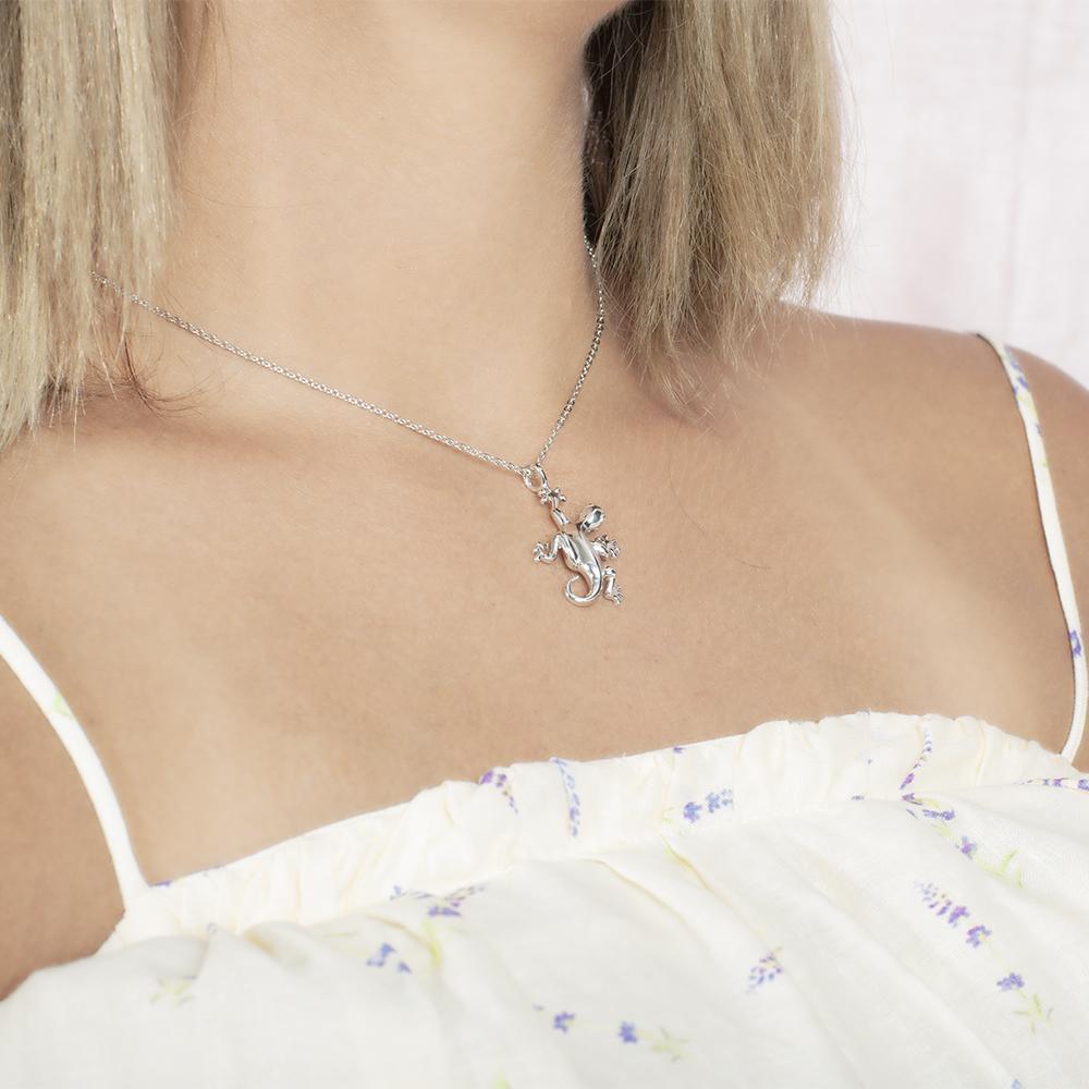 In this photo there is a model turned to the right with blonde hair and a white shirt with purple flowers, wearing a sterling silver gecko pendant.