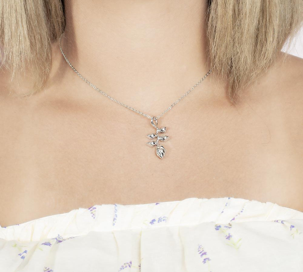 In this picture there is a model with blonde hair and a white shirt with purple flowers wearing a sterling silver heliconia pendant.