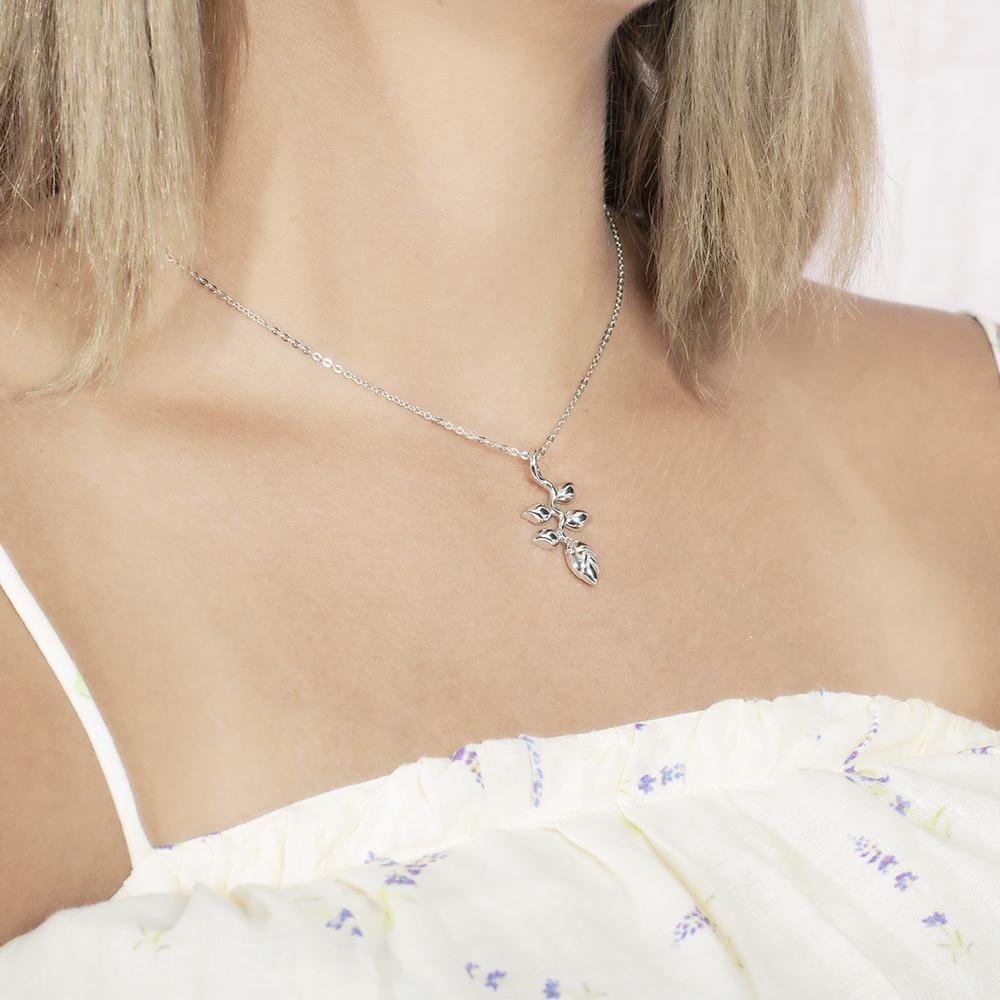 In this picture there is a model with blonde hair and a white shirt with purple flowers turned to the right wearing a sterling silver heliconia pendant.