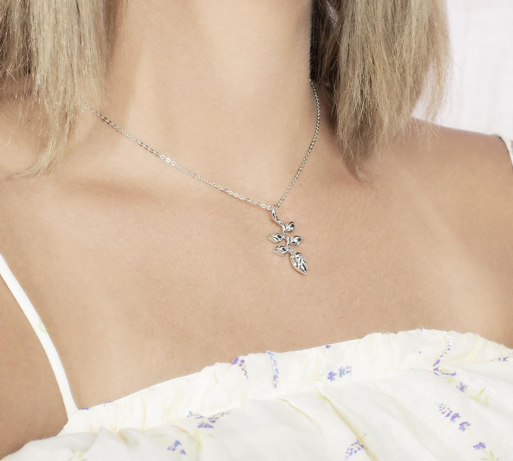 In this picture there is a model with blonde hair and a white shirt with purple flowers turned to the right wearing a sterling silver heliconia pendant.
