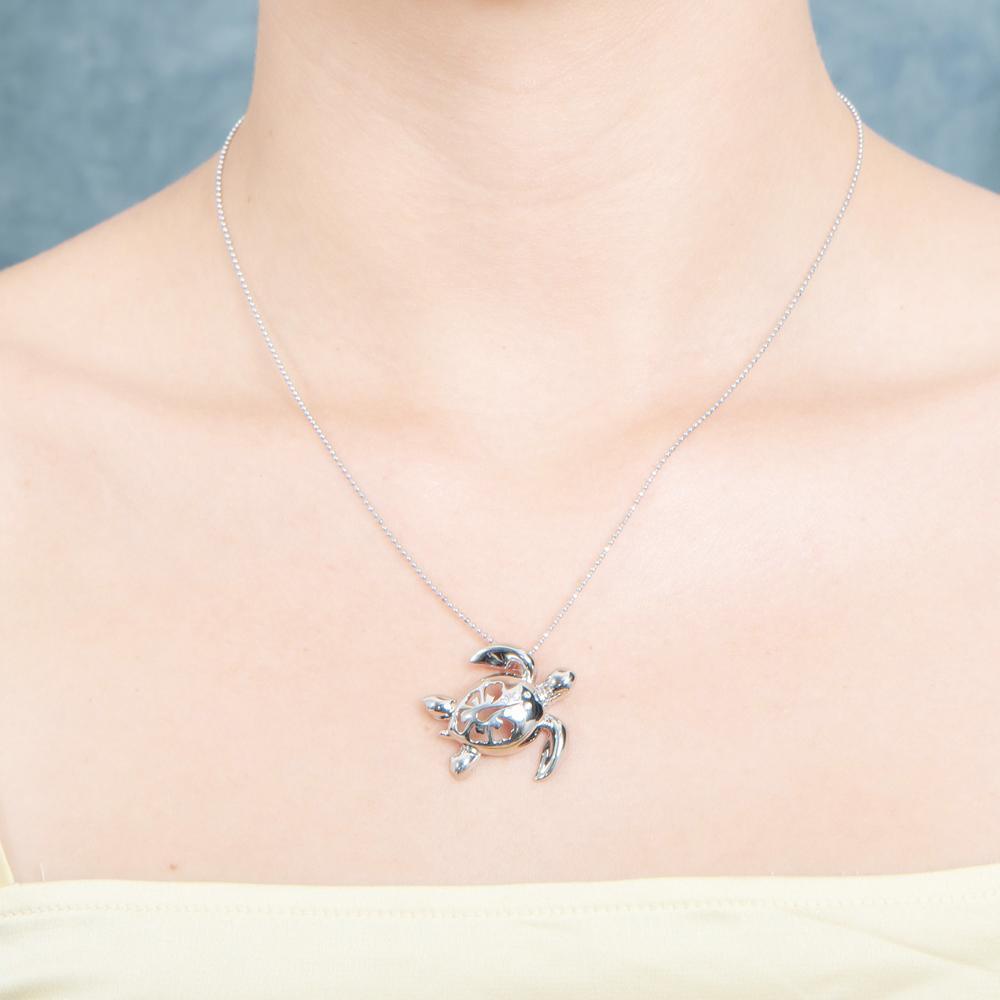 The picture shows a model wearing a 925 sterling silver sea turtle pendant with hibiscus cut-out and cubic zirconia.