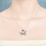 The picture shows a model wearing a 925 sterling silver sea turtle pendant with hibiscus cut-out and cubic zirconia.