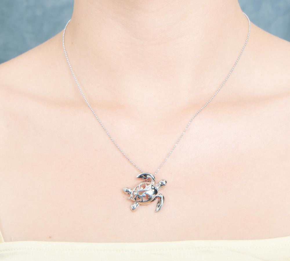 The picture shows a model wearing a 925 sterling silver sea turtle pendant with hibiscus cut-out and cubic zirconia.