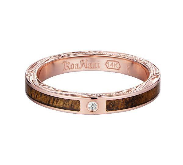 In this photo there is a rose gold koa wood ring with hand engravings of scrolls and one diamond.