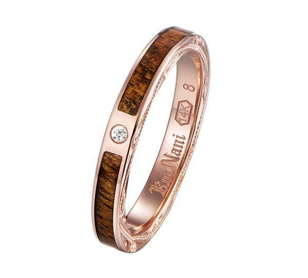 In this photo there is a rose gold koa wood ring with hand engravings of scrolls and one diamond.