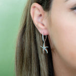 The picture shows a model wearing a 925 sterling silver starfish lever-back earring with topaz