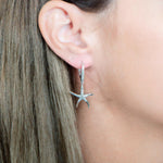 The picture shows a model wearing a 925 sterling silver starfish lever-back earring with topaz