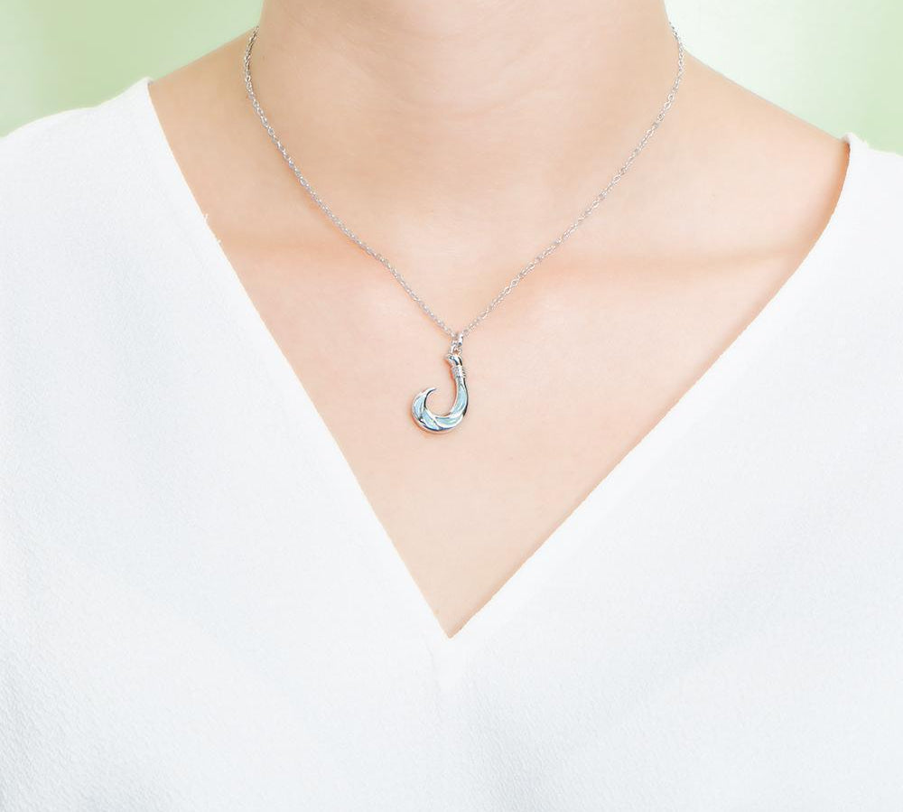 In this photo there is a model with a white shirt wearing a sterling silver fish hook pendant with blue larimar gemstones.