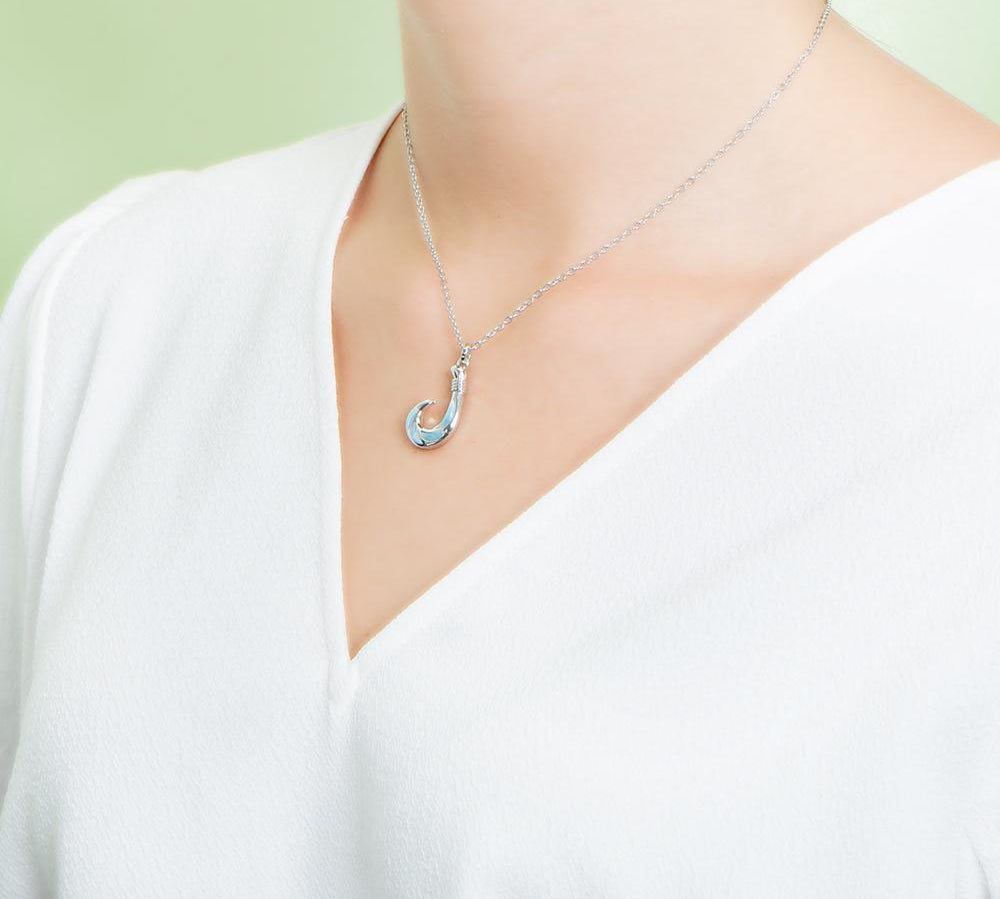 In this photo there is a model with a white shirt turned to the left, wearing a sterling silver fish hook pendant with blue larimar gemstones.