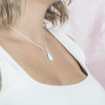 The picture shows a model wearing a 925 sterling silver larimar teardrop pendant with aquamarine and cubic zirconia.