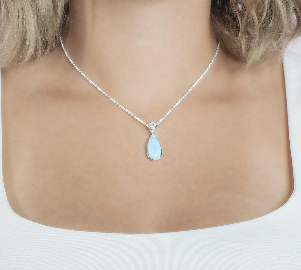 The picture shows a model wearing a 925 sterling silver larimar teardrop pendant with aquamarine and cubic zirconia.