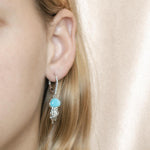 The picture shows a model wearing a 925 sterling silver larimar jellyfish lever back earring with topaz