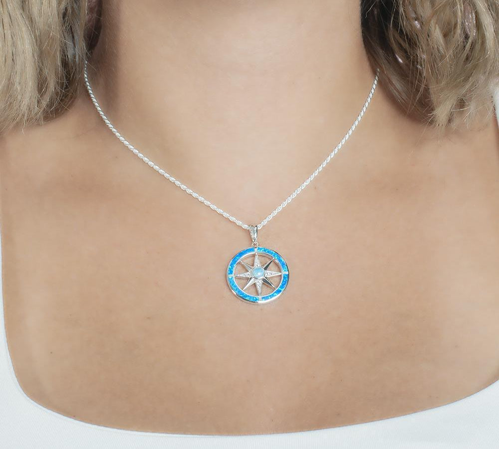 In this photo there is a model with blonde hair and a white shirt, wearing a sterling silver compass pendant with blue larimar, blue opalite, and topaz gemstones.