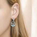 The picture shows a model wearing a 925 sterling silver larimar dolphin cove earring with topaz