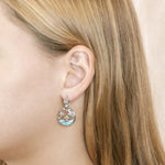 The picture shows a model wearing a 925 sterling silver larimar dolphin cove earring with topaz