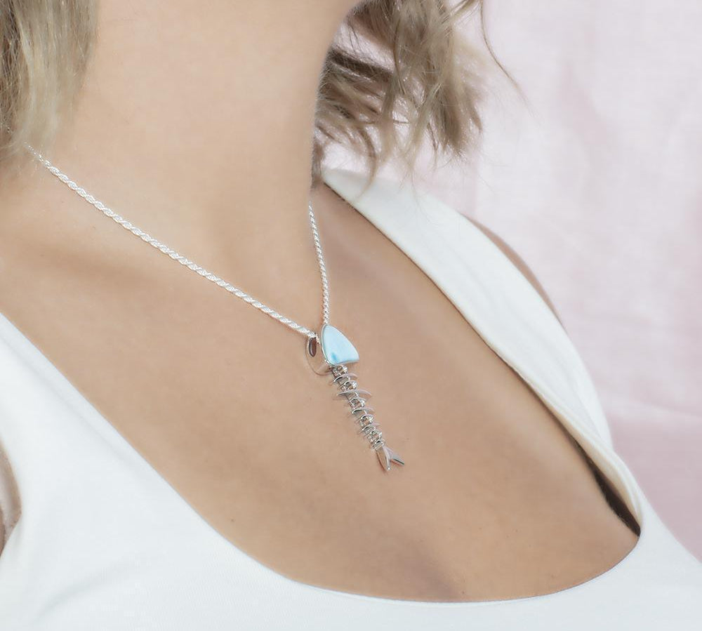The picture shows a model wearing a 925 sterling silver larimar fish bone pendant with cubic zirconia.