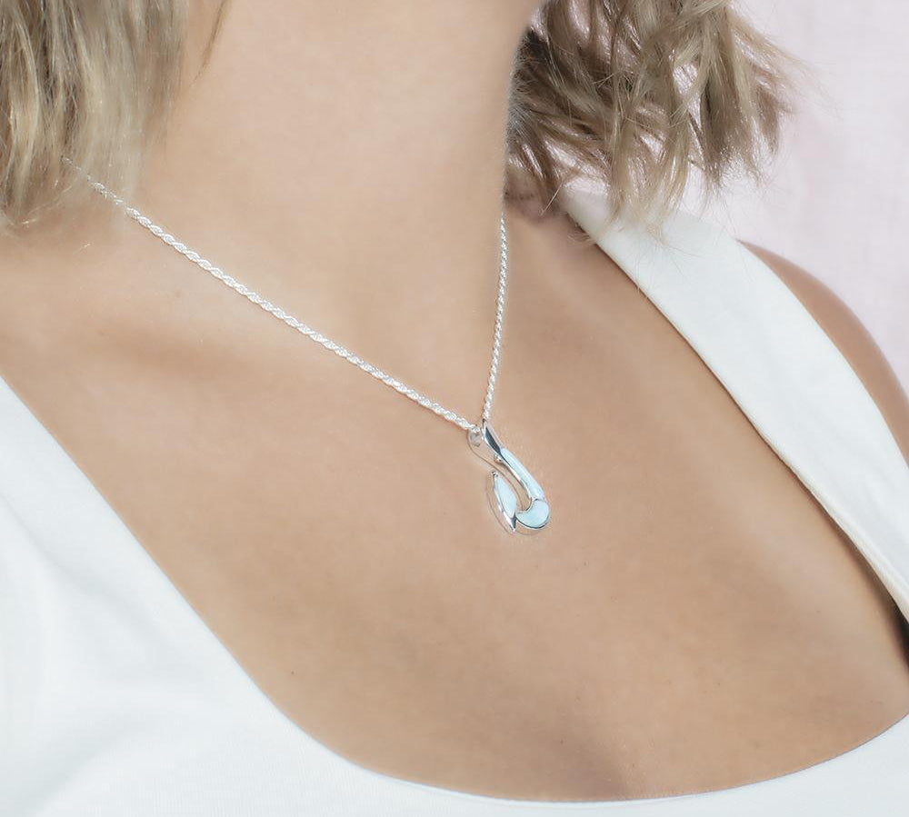 In this photo there is a model with blonde hair and a white shirt turned to the right, wearing a sterling silver fish hook pendant with blue larimar gemstones.