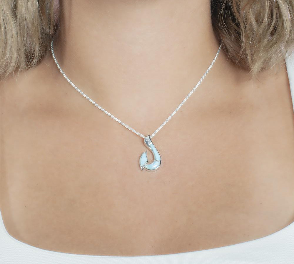 In this photo there is a model with blonde hair and a white shirt, wearing a sterling silver fish hook pendant with blue larimar gemstones.