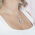 The picture shows a model wearing a 925 sterling silver teardrop shaped pendant with 3 sea turtles in the center with cubic zirconia and larimar.