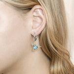 In this photo there is a model wearing 925 sterling silver hummingbird lever-back earrings with blue larimar and topaz gemstones.