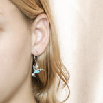 In this photo there is a model wearing 925 sterling silver hummingbird lever-back earrings with blue larimar and topaz gemstones.