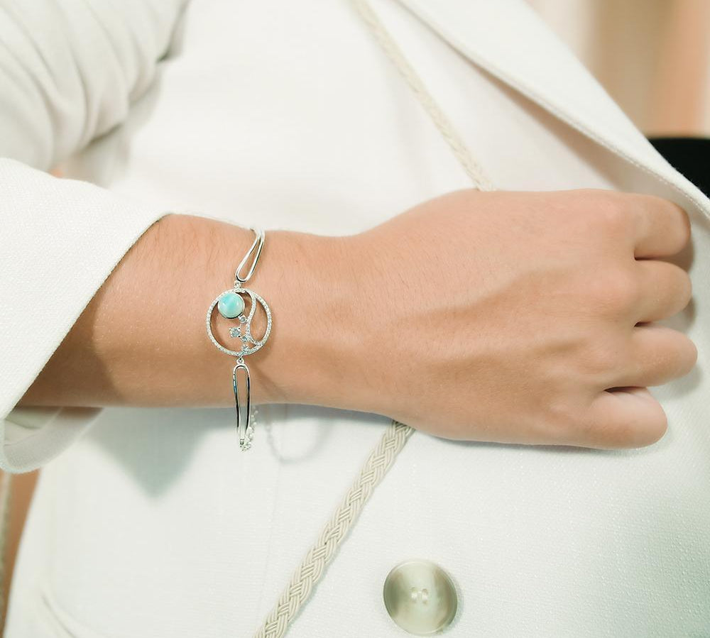 In this photo there is a model wearing a 925 sterling silver bracelet with a wave and sun design with larimar, topaz, and aquamarine gemstones.