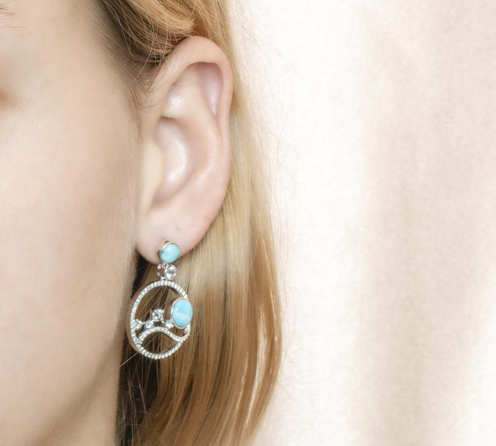 In this photo there is a model wearing 925 sterling silver earrings with blue larimar, aquamarine, and topaz gemstones.