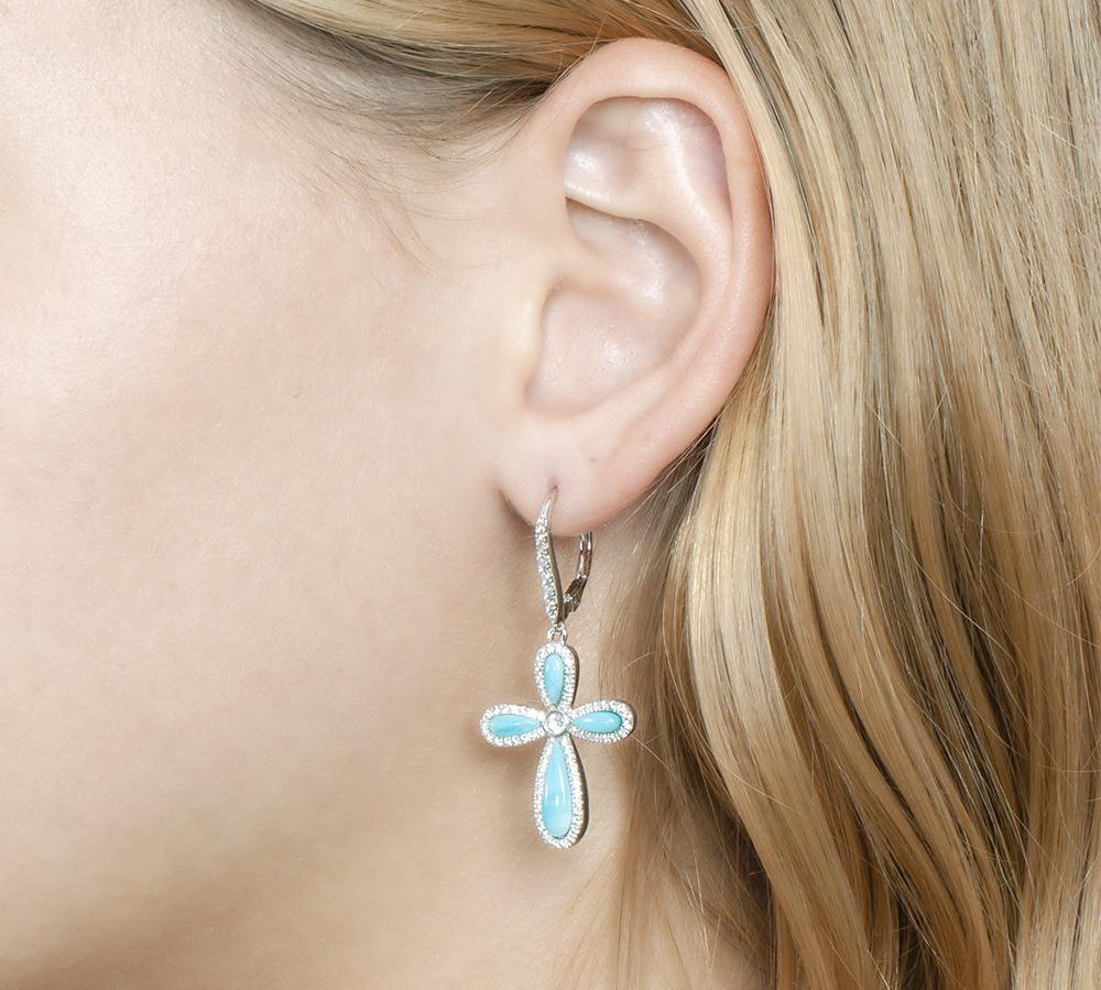 The picture shows a model wearing a 925 sterling silver larimar cross lever-back earring with topaz.