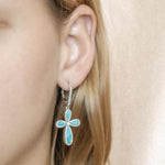 The picture shows a model wearing a 925 sterling silver larimar cross lever-back earring with topaz.
