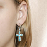 The picture shows a model wearing a 925 sterling silver larimar cross lever-back earring with topaz.