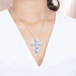 The picture shows a model wearing a 925 sterling silver larimar cross pendant with topaz.