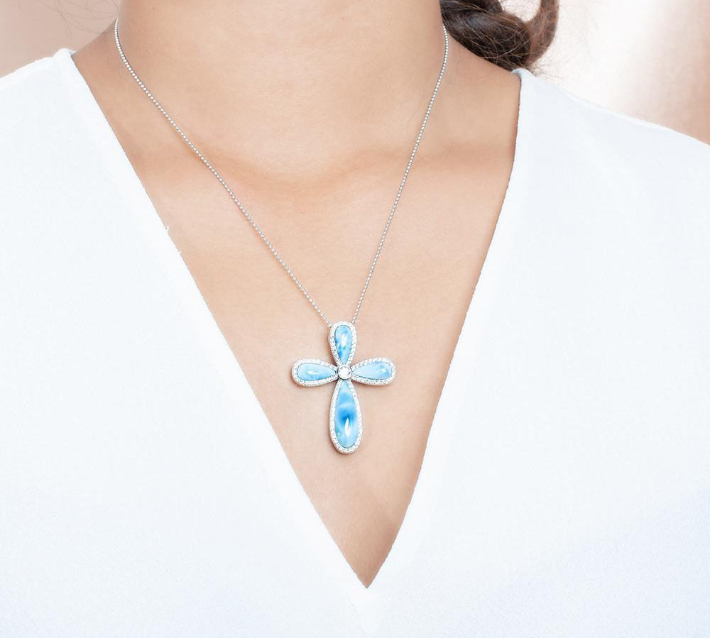The picture shows a model wearing a 925 sterling silver larimar cross pendant with topaz.