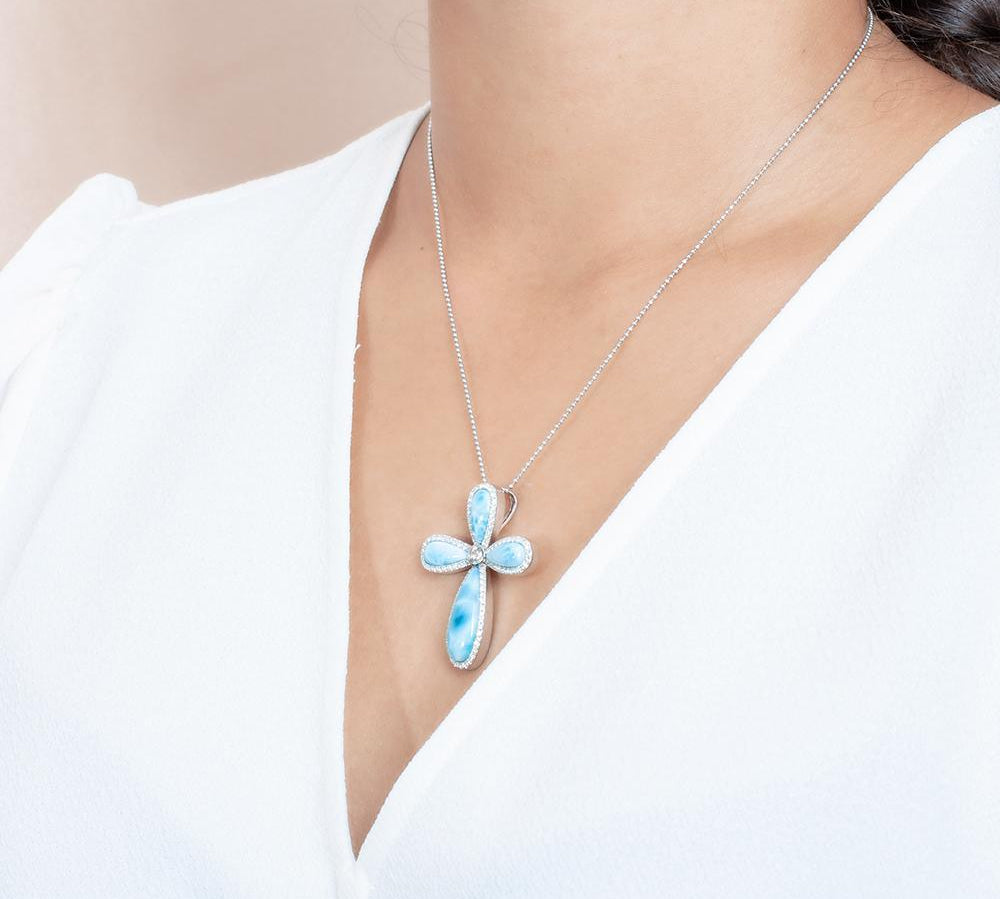 The picture shows a model wearing a 925 sterling silver larimar cross pendant with topaz.
