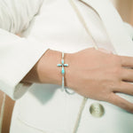The picture shows a model wearing a 925 sterling silver larimar cross bracelet with topaz.