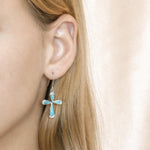 The picture shows a model wearing a 925 sterling silver larimar cross earring with topaz.