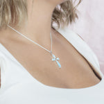 The picture shows a model wearing a 925 sterling silver larimar cross pendant with topaz.