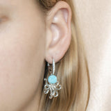 The picture shows a model wearing a 925 sterling silver larimar octopus lever-back earring with topaz and aquamarine gemstones.