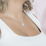 The picture shows a model wearing a 925 sterling silver larimar teardrop pendant with topaz.