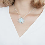 The picture shows a model wearing a 925 sterling silver larimar living sand dollar pendant.