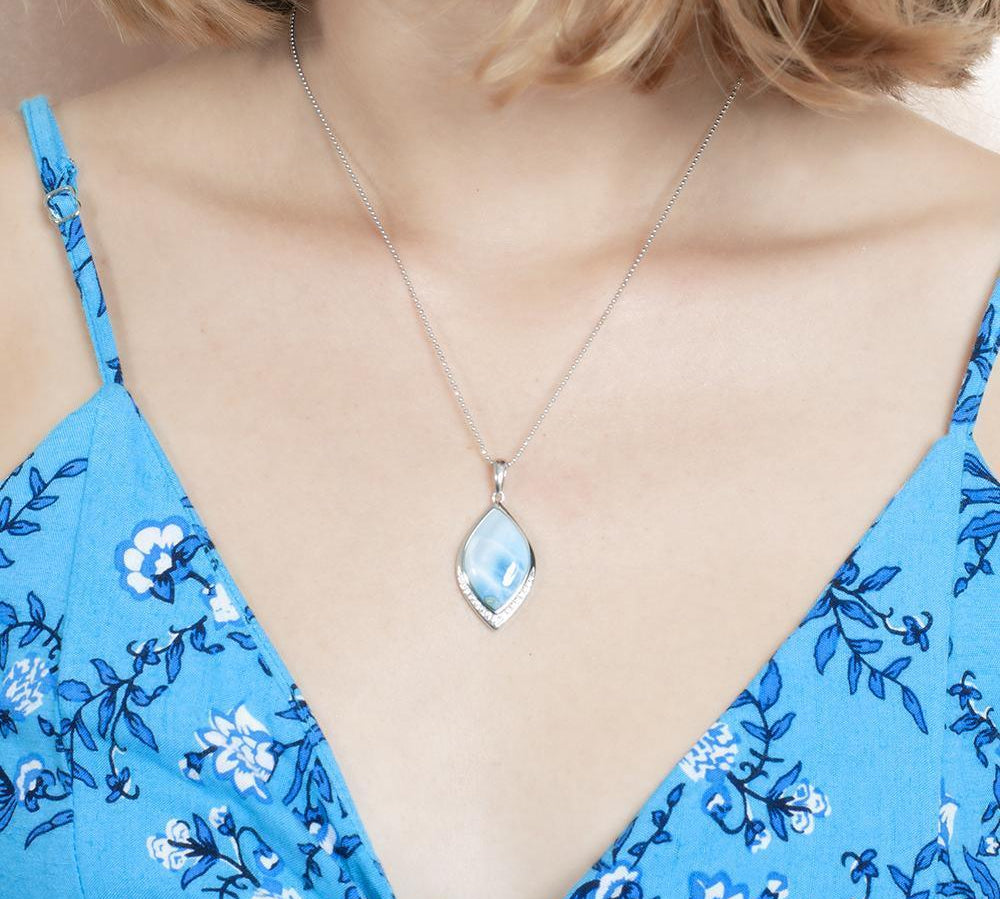 The picture shows a model wearing a blue dress and a 925 sterling silver larimar loa mandorla pendant with topaz.
