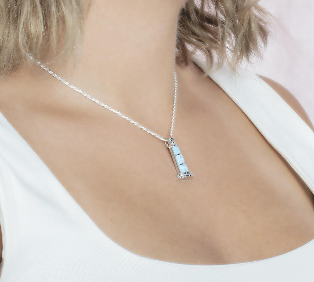 In this picture there is a model with blonde hair and a white shirt turned to the right wearing a lighthouse pendant with blue larimar gemstones set in sterling silver.
